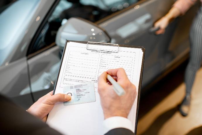 Firma de documentos junto a un carné de conducir mientras de fondo un conductor se sube al coche de fondo