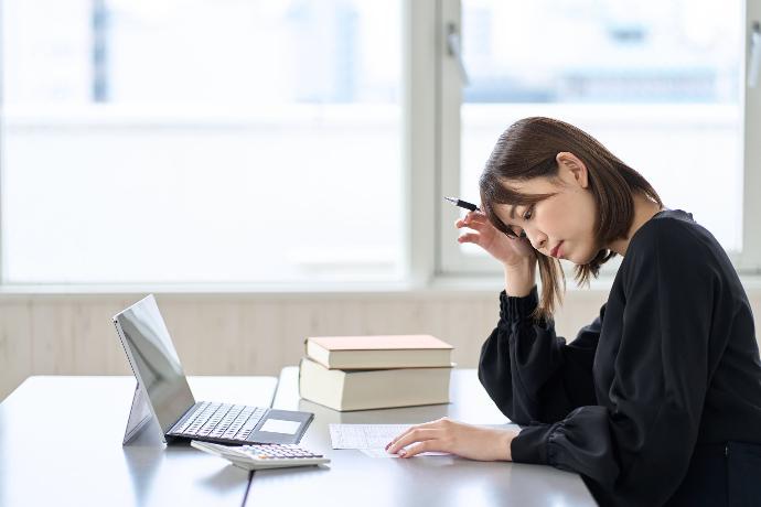 Mujer concrentrada revisando documento en su mesa enfrente del ordenador y calculadora